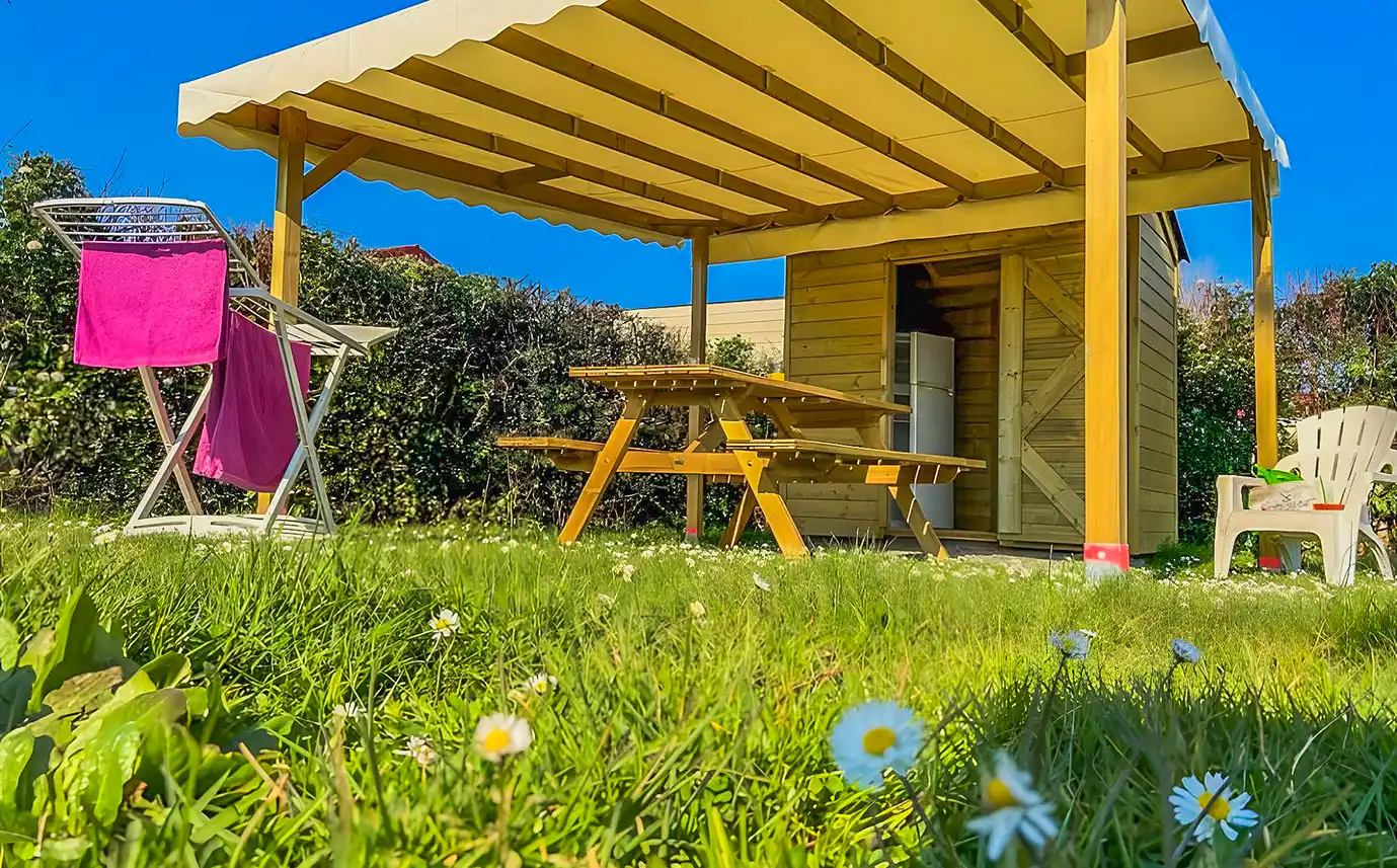 Espace couvert d’un emplacement Privilège Garden avec table, réfrigérateur et étendoir, camping en Vendée